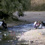 By the river, women talk to each other while their washing dries on a tree.