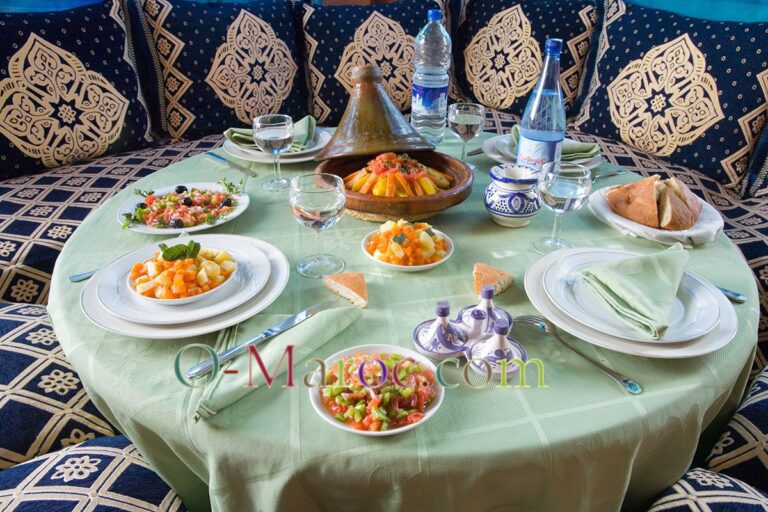 Dining table, green tablecloth, blue cushions, tagines and salads
