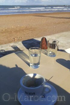 A cup of coffee and a glass of water in front of the sea