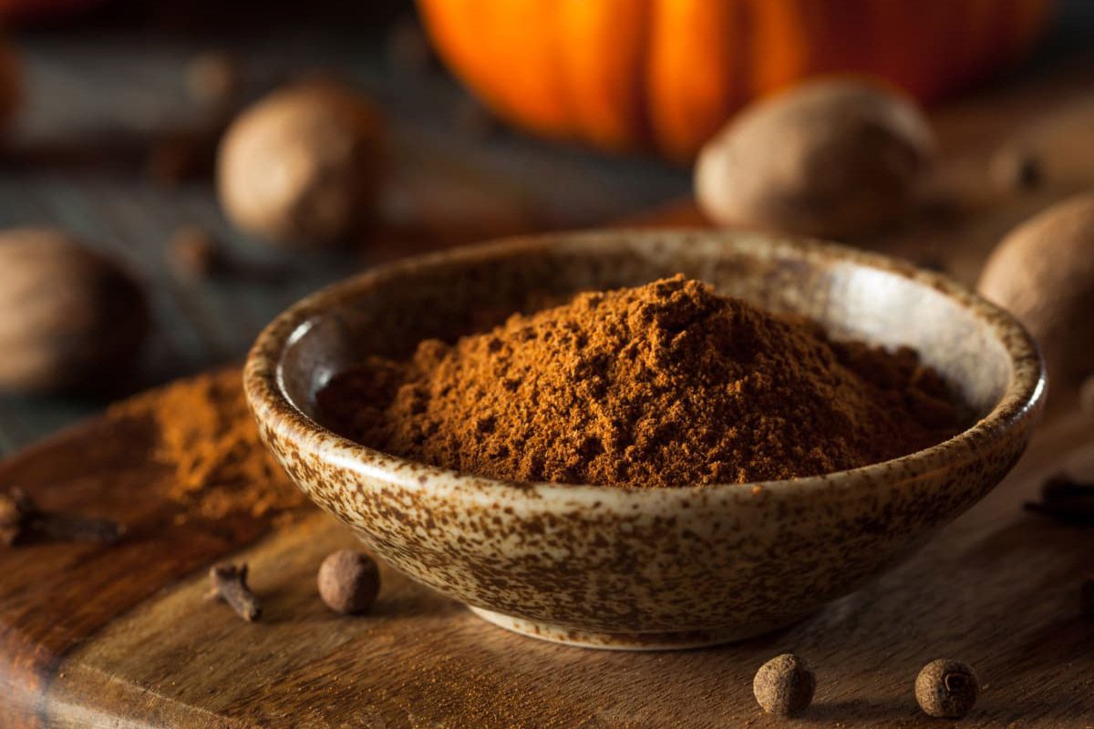 Ground nutmeg in a bowl front of a pumpkin