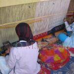 Two women in front of a traditional loom