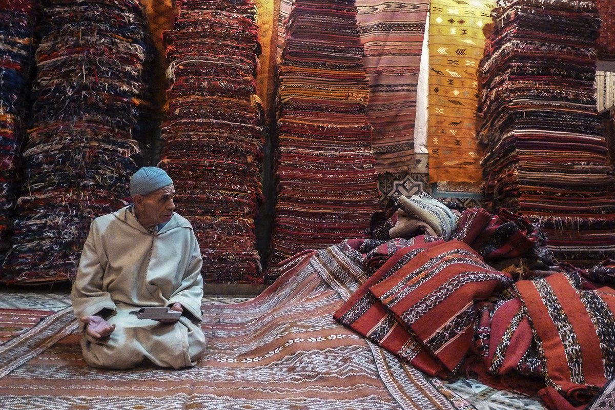 Rug salesman in his shop, with piles of rugs and a calculator