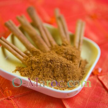 Cinnamon powder and cinnamon stick in a small dish on an orange cloth