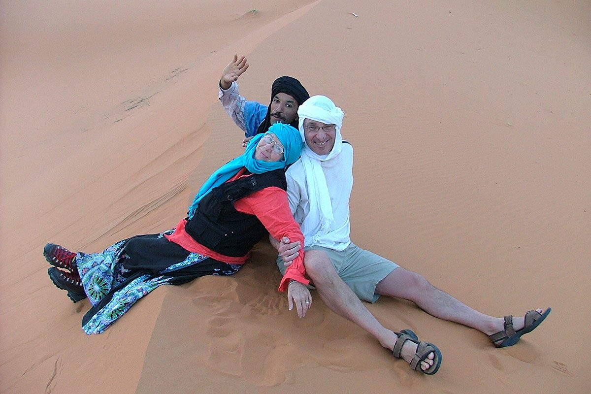 Un guide et deux touristes en haut d'une dune à Merzouga